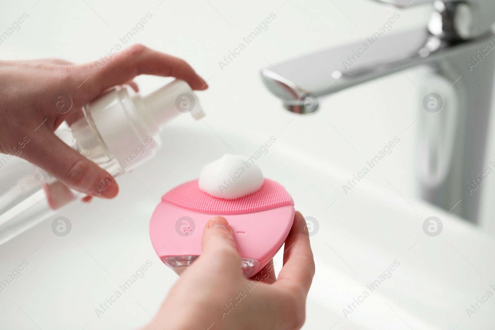 Photo of Washing face. Woman applying cleansing foam onto brush above sink in bathroom, closeup