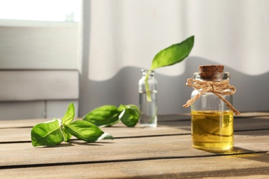 Photo of Bottle of essential basil oil on table against blurred background. Space for text