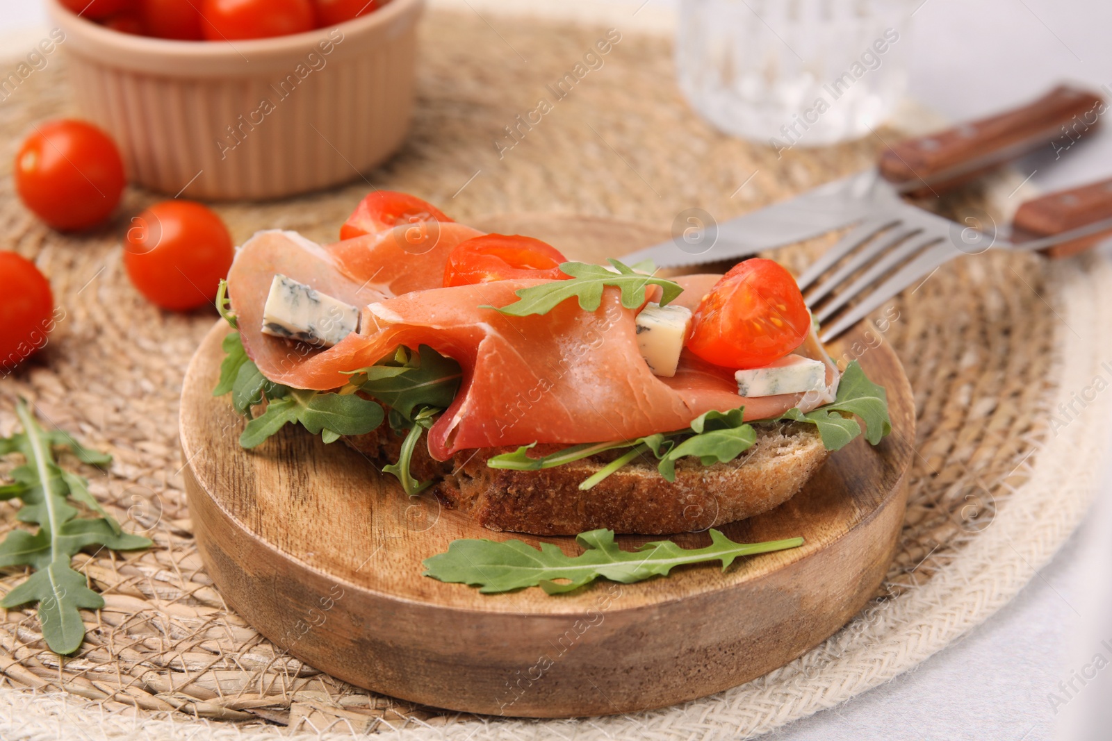 Photo of Tasty bruschetta with prosciutto, arugula, cheese and tomato on wooden board