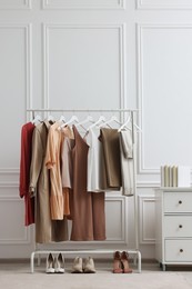 Photo of Rack with different stylish women`s clothes and shoes near white wall indoors