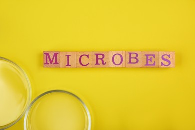 Photo of Word Microbes made with wooden cubes and magnifying glass on yellow background, top view