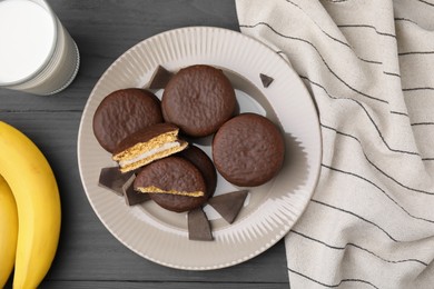 Photo of Tasty banana choco pies, pieces of chocolate, milk and fruits on grey wooden table, flat lay