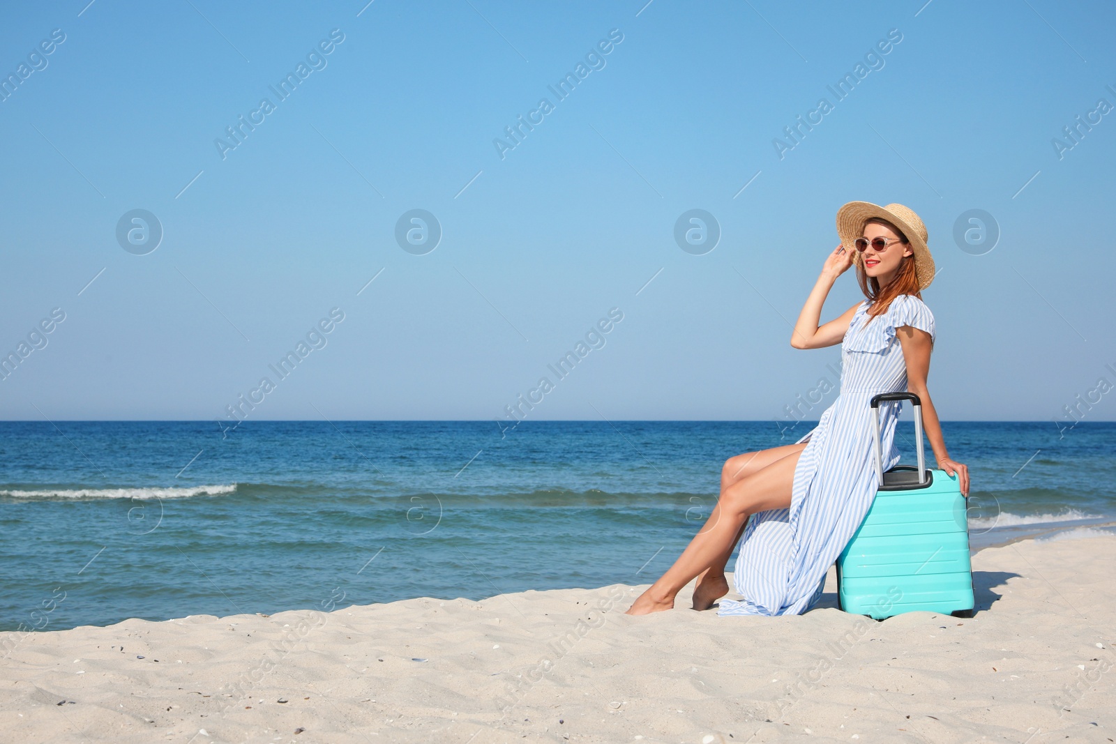 Photo of Beautiful woman with suitcase on sandy beach near sea