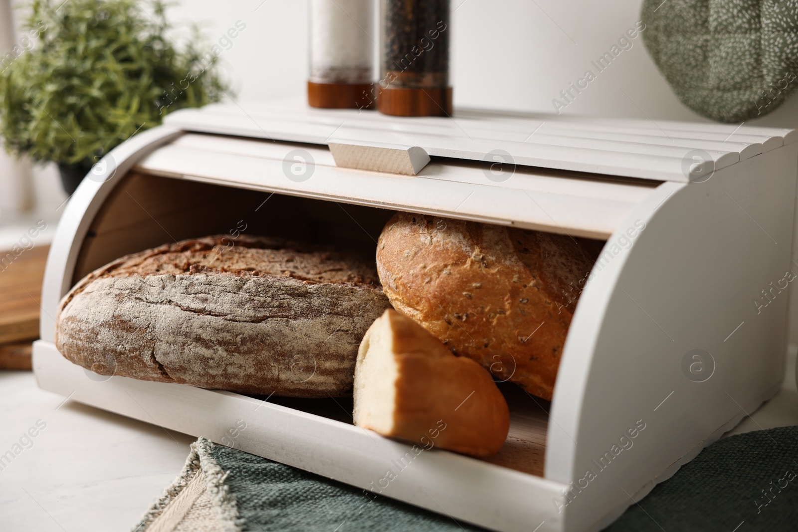 Photo of Wooden bread basket with freshly baked loaves on white marble table in kitchen