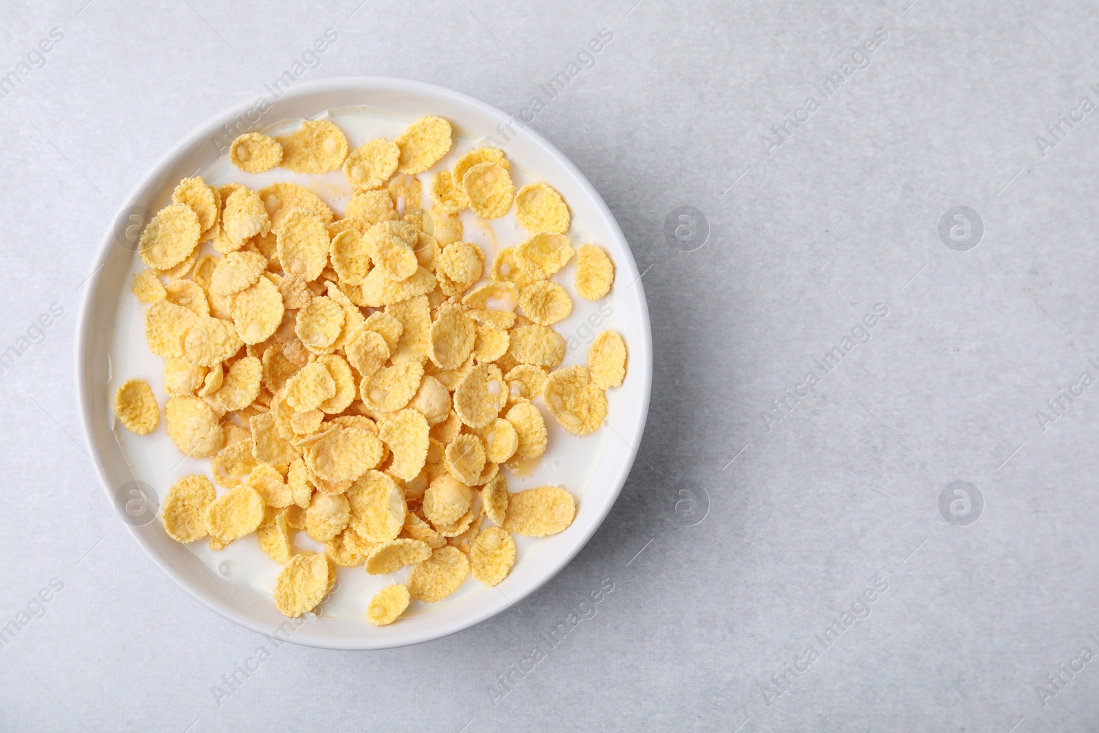 Photo of Breakfast cereal. Corn flakes and milk in bowl on light grey table, top view. Space for text