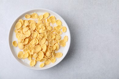 Photo of Breakfast cereal. Corn flakes and milk in bowl on light grey table, top view. Space for text