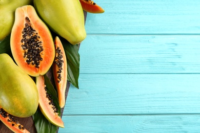 Photo of Fresh ripe papaya fruits with green leaves on turquoise wooden table, flat lay. Space for text