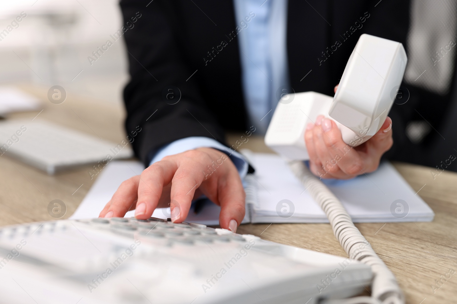 Photo of Secretary dialing number on telephone at table in office, closeup