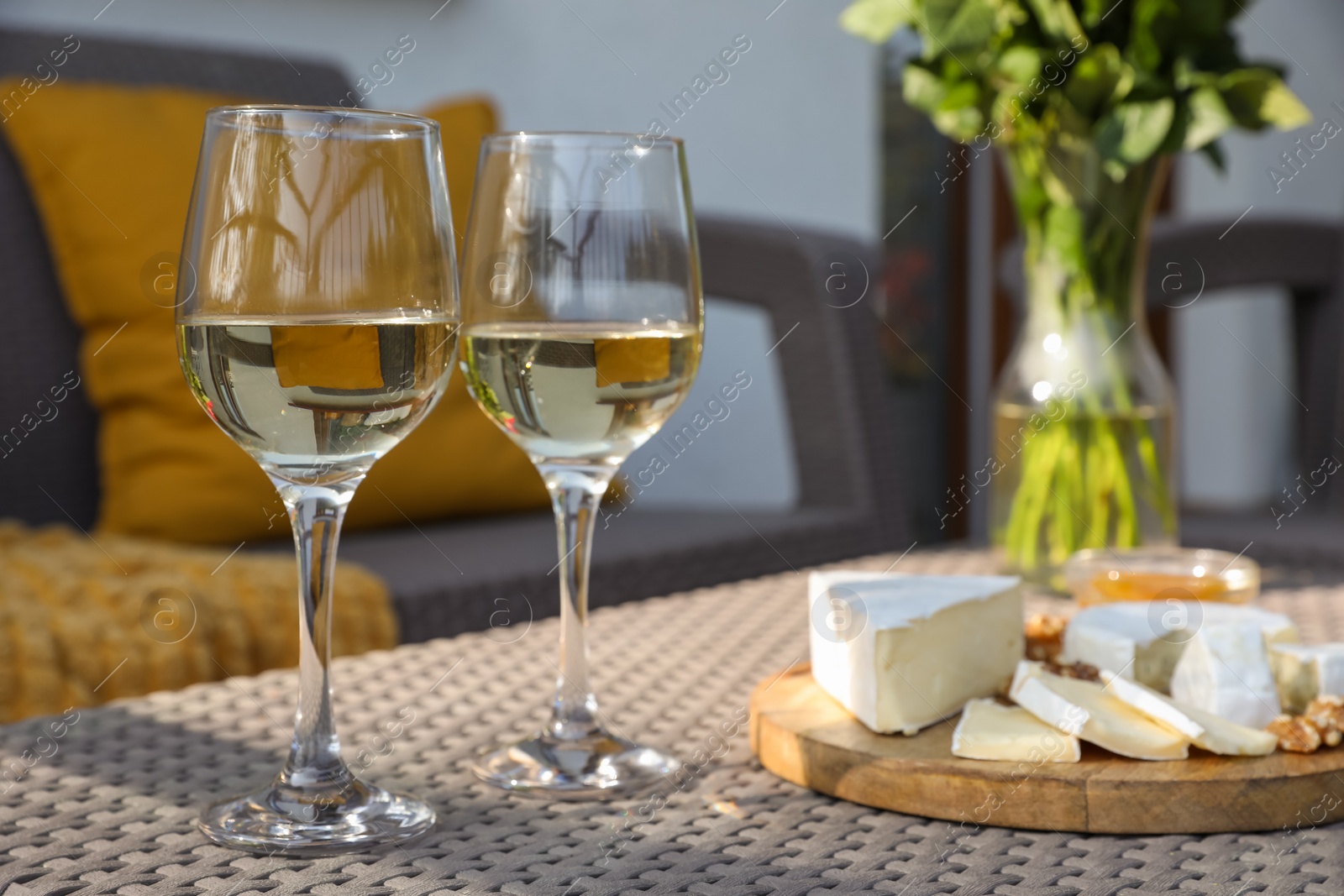 Photo of Glasses of wine, snacks and vase with flowers on rattan table at balcony, closeup