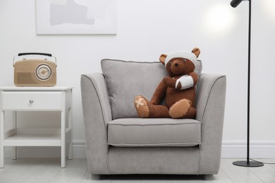 Photo of Toy bear with bandages sitting in armchair indoors