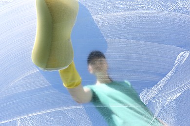 Woman cleaning glass with sponge on sunny day