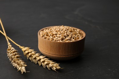 Dried ears of wheat and grains in wooden bowl on black table