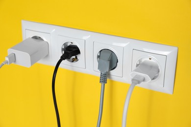 Photo of Power sockets with inserted plugs on yellow wall, closeup. Electrical supply