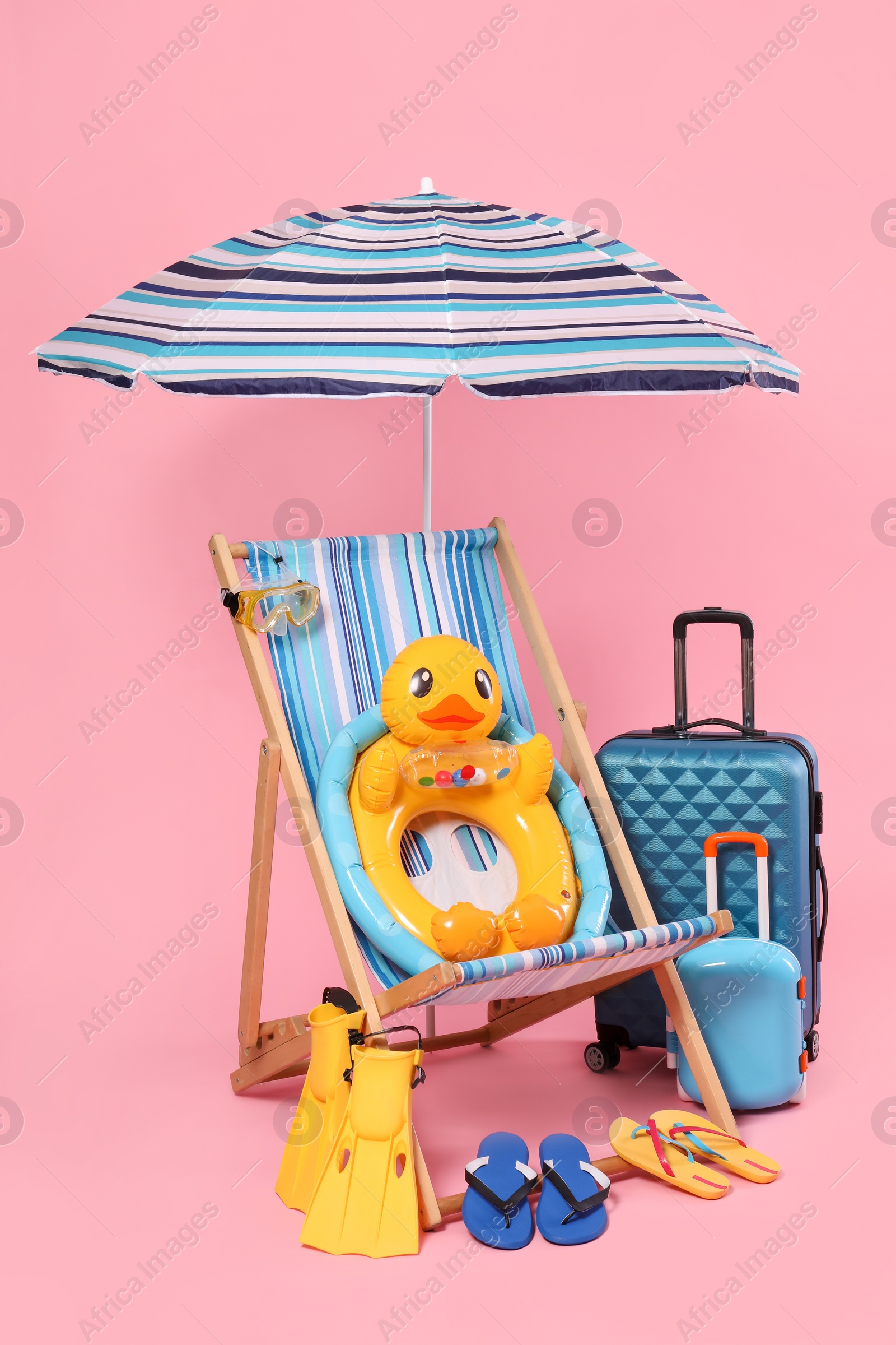 Photo of Deck chair, suitcases and beach accessories on pink background