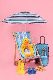 Photo of Deck chair, suitcases and beach accessories on pink background