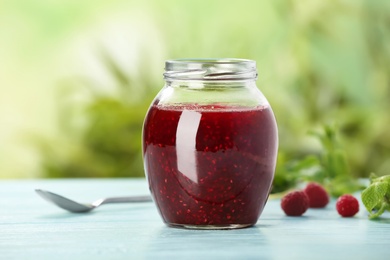 Photo of Jar with delicious raspberry jam on table against blurred background