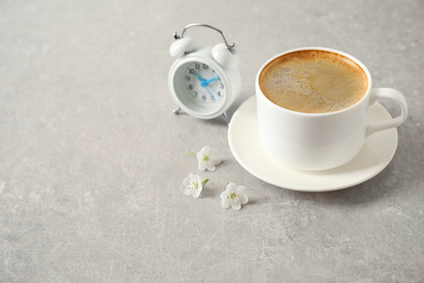 Photo of Cup of morning coffee, flowers and alarm clock on light grey table. Space for text