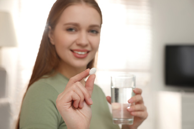 Photo of Woman with glass of water and vitamin pill indoors, focus on hand