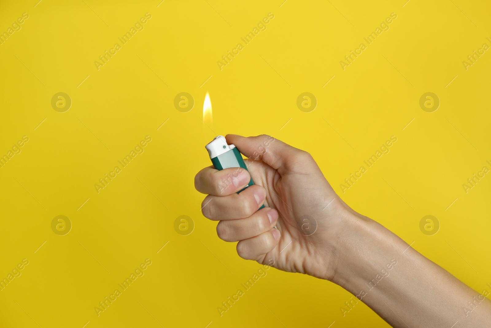 Photo of Woman holding green lighter on yellow background, closeup