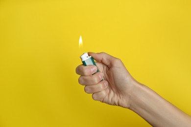 Photo of Woman holding green lighter on yellow background, closeup