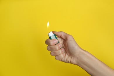 Woman holding green lighter on yellow background, closeup