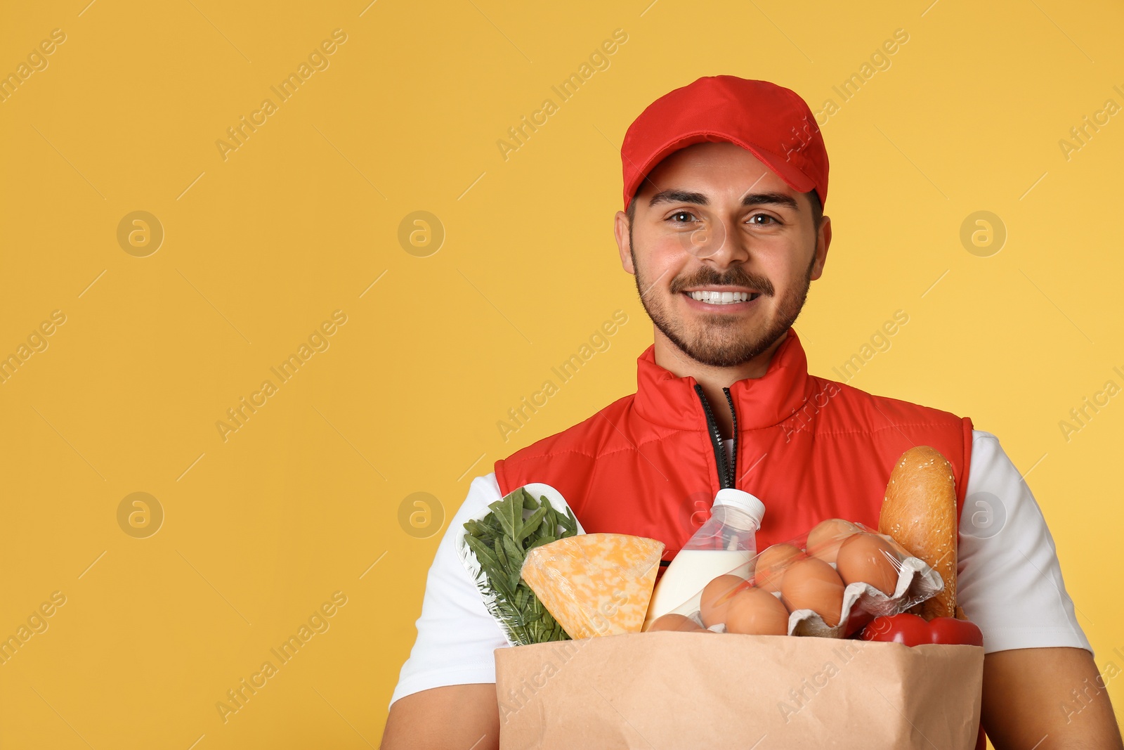 Photo of Food delivery courier holding paper bag with products on color background. Space for text