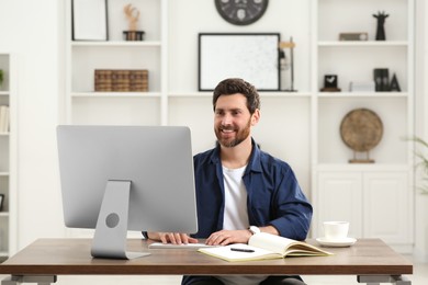 Photo of Home workplace. Happy man working with computer at wooden desk in room