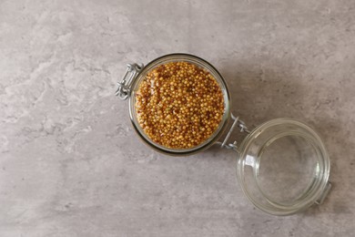 Photo of Jar of delicious whole grain mustard on grey table, top view. Space for text