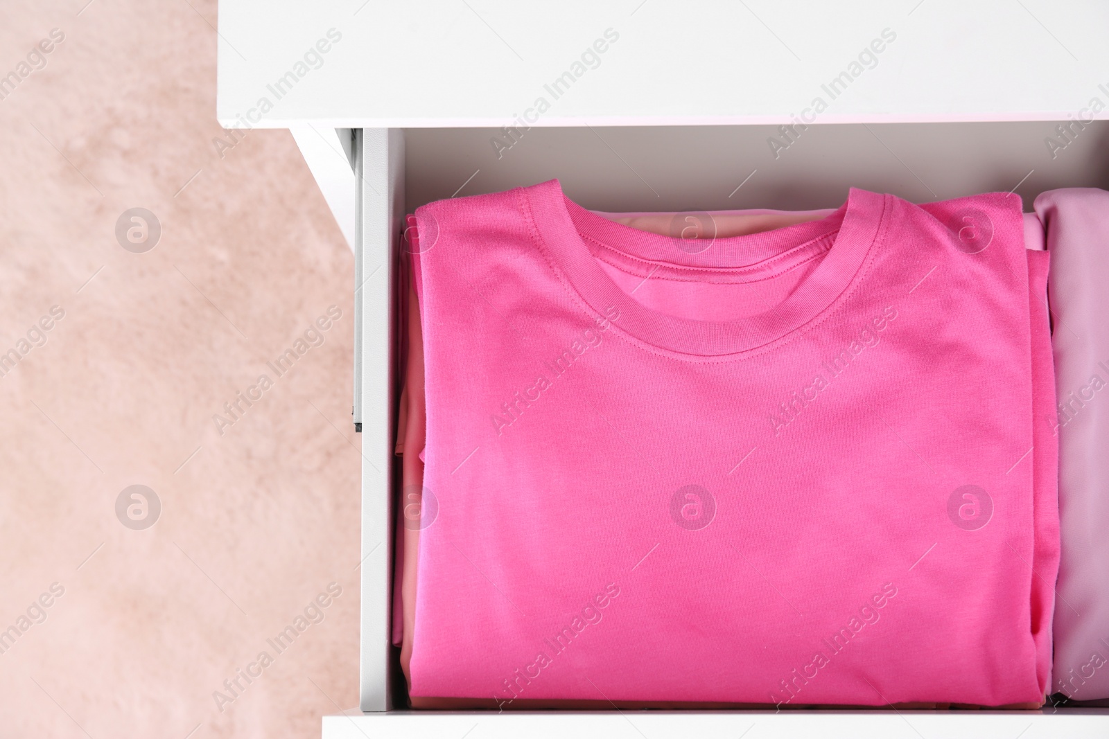 Photo of Folded pink clothes in white chest of drawers indoors, top view