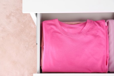 Folded pink clothes in white chest of drawers indoors, top view