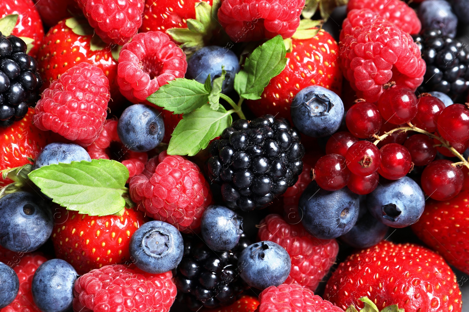 Photo of Assortment of fresh ripe berries with green leaves as background, top view