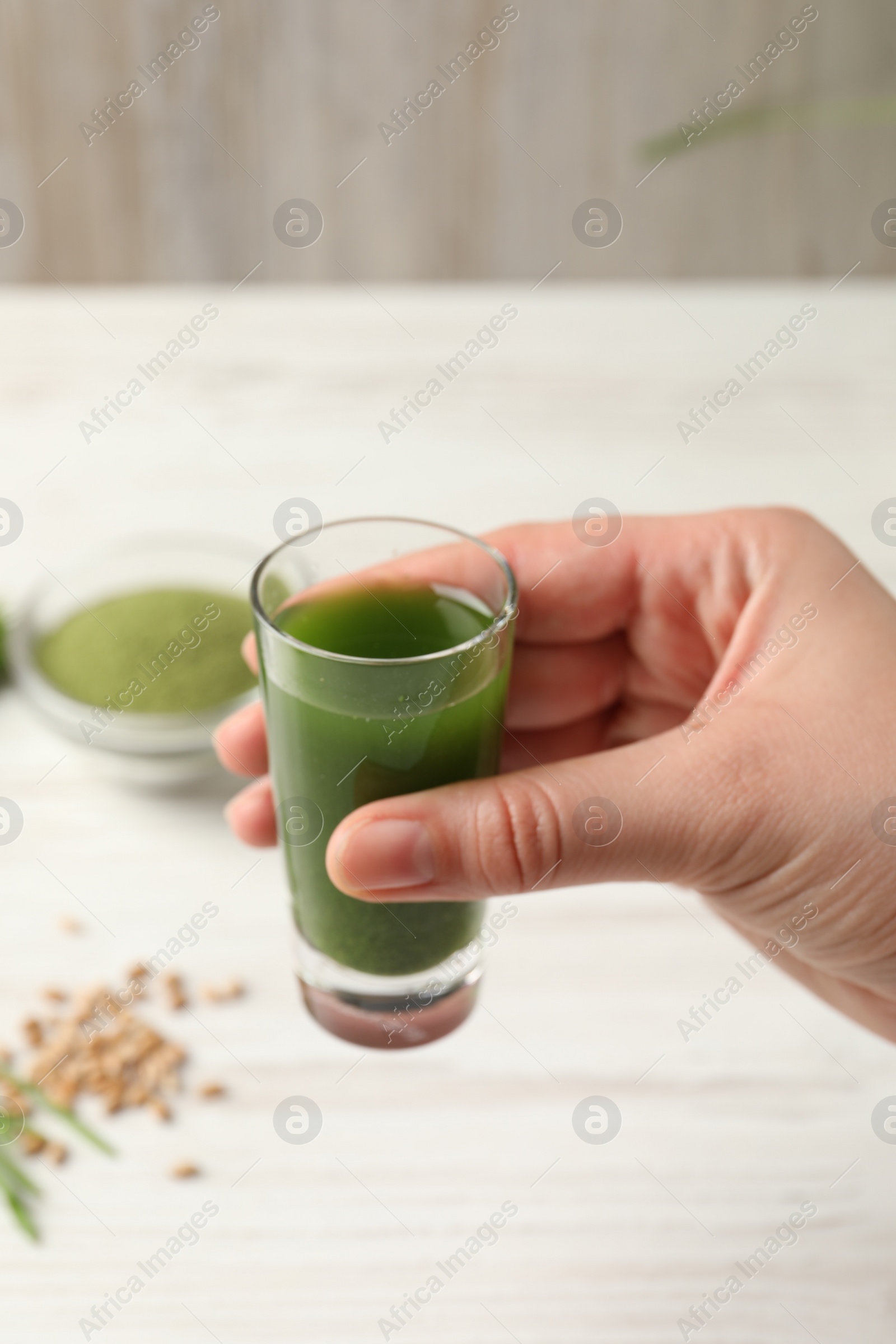 Photo of Woman holding glass of wheat grass drink at white table, closeup