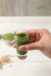 Woman holding glass of wheat grass drink at white table, closeup