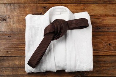 Brown karate belt and white kimono on wooden background, top view