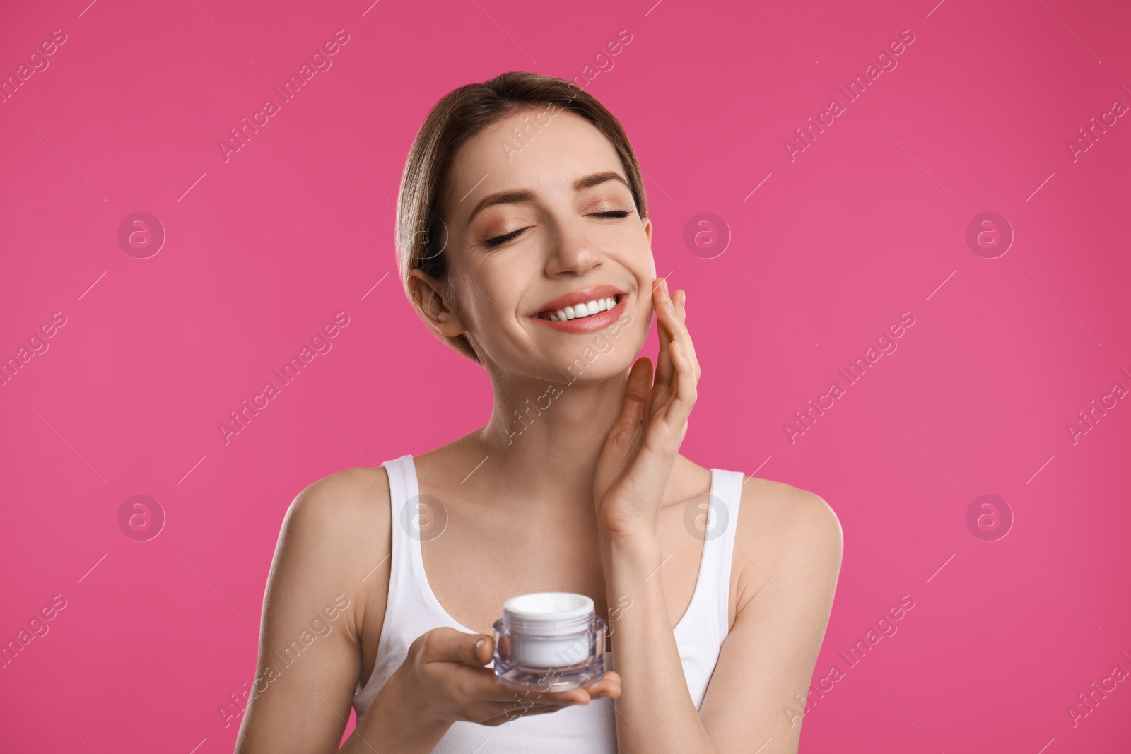 Photo of Young woman applying facial cream on pink background