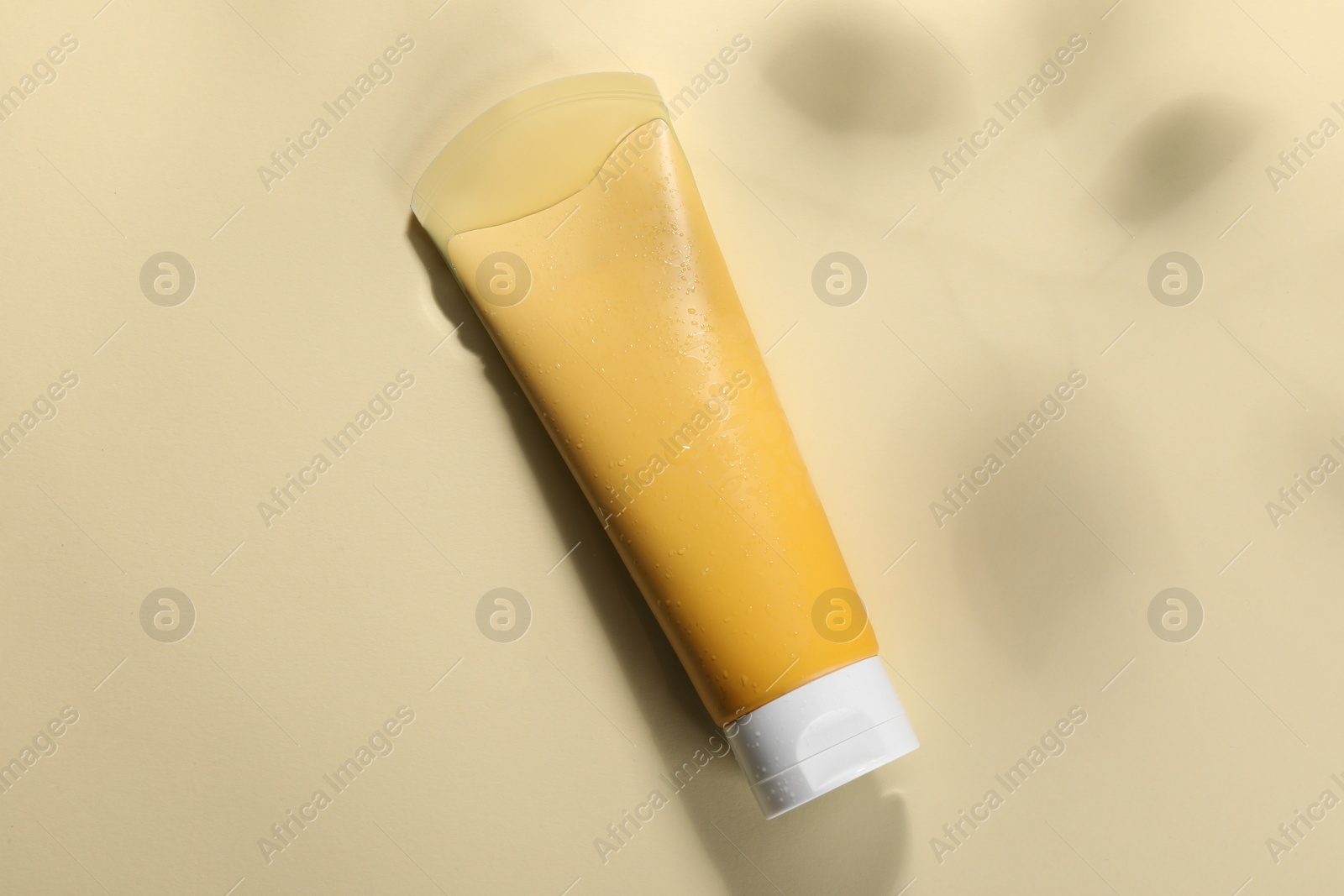 Photo of Tube of face cleansing product in water against beige background, top view