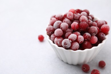 Photo of Frozen red cranberries in bowl on light table, closeup. Space for text