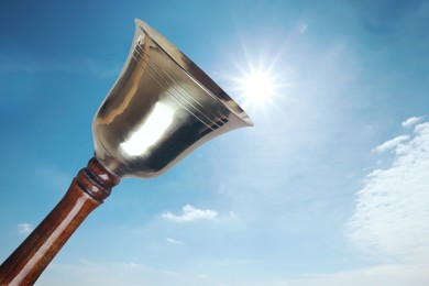 Image of Shiny school bell with wooden handle against blue sky