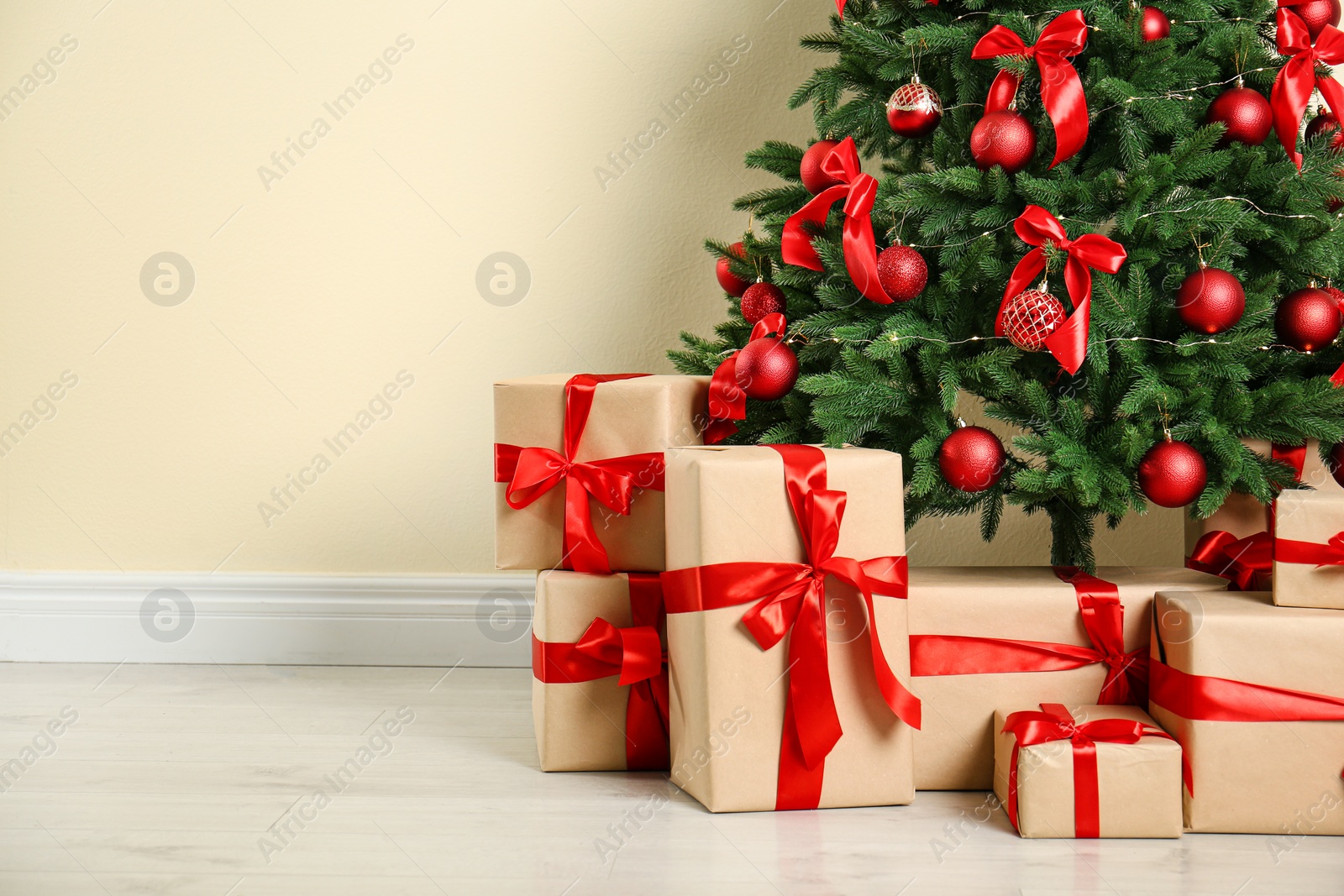 Photo of Decorated Christmas tree and gift boxes near beige wall. Space for text