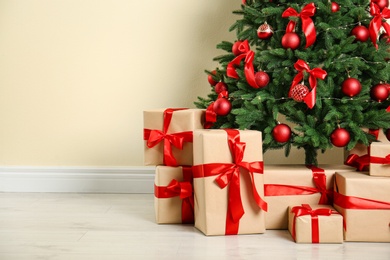 Photo of Decorated Christmas tree and gift boxes near beige wall. Space for text