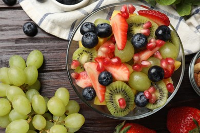 Photo of Tasty fruit salad in bowl and ingredients on wooden table, flat lay