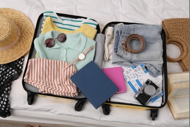 Open suitcase with clothes and accessories on bed, flat lay