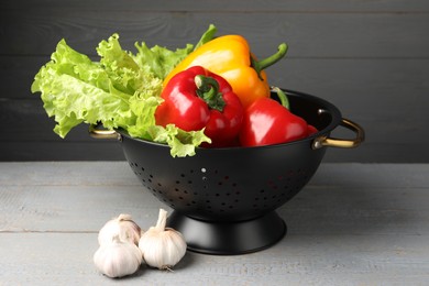 Photo of Black colander and different vegetables on rustic wooden table