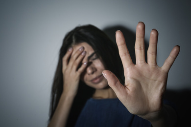 Photo of Crying young woman making stop gesture near white wall, focus on hand. Domestic violence concept