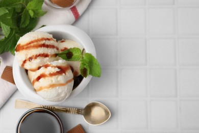 Scoops of tasty ice cream with mint, candies and caramel sauce on white tiled table, flat lay. Space for text