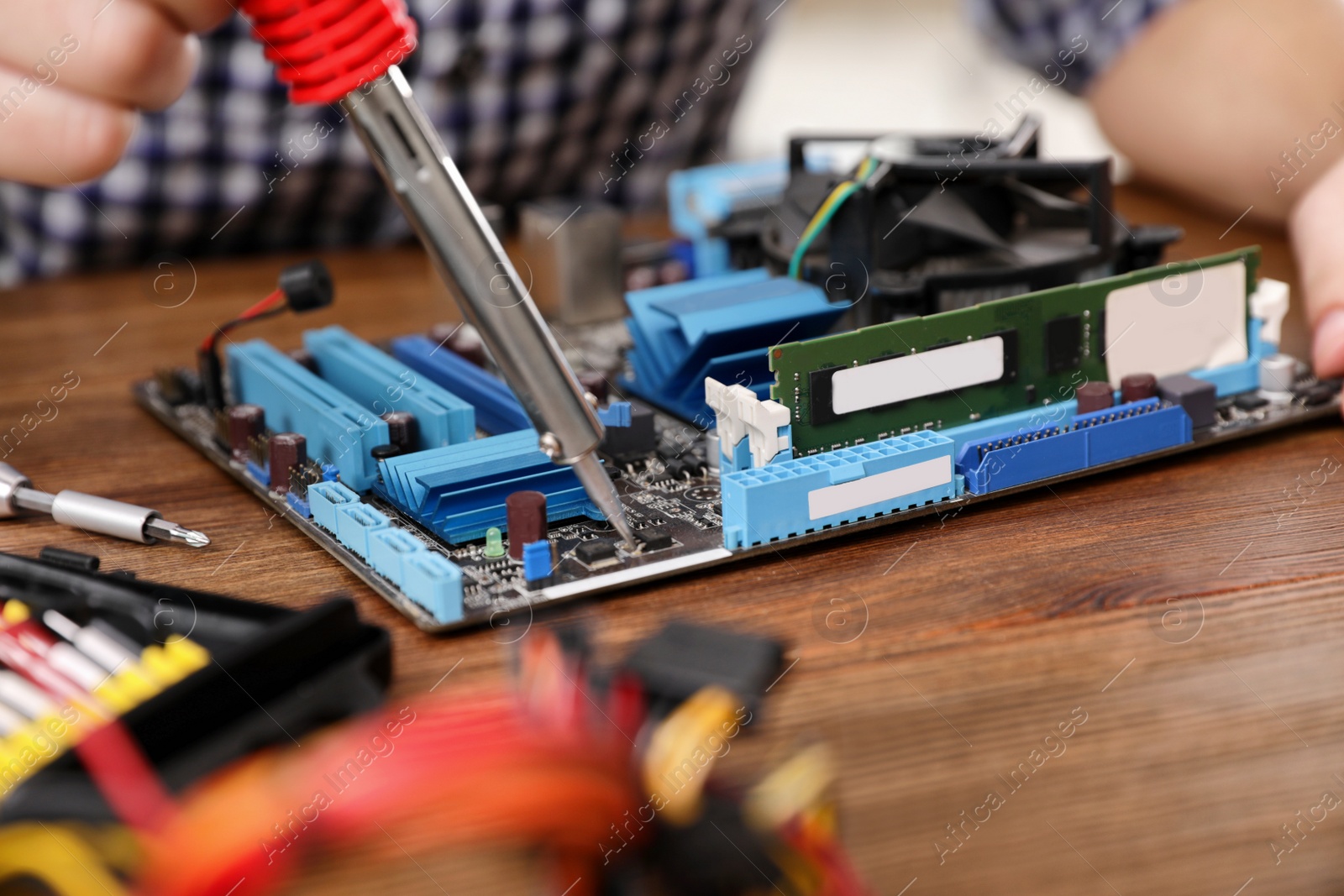 Photo of Male technician repairing motherboard with soldering iron at table, closeup