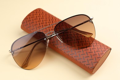 Photo of Stylish sunglasses and brown leather case with pattern on beige background