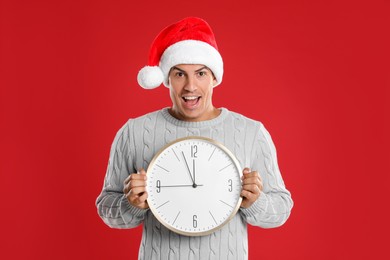 Photo of Man in Santa hat with clock on red background. New Year countdown