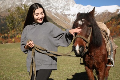 Photo of Young woman stroking horse in mountains on sunny day. Beautiful pet