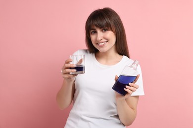 Young woman with mouthwash on pink background